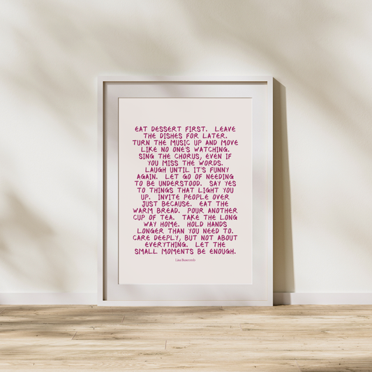 Framed print with pink text on a white background, leaning against a beige wall.
